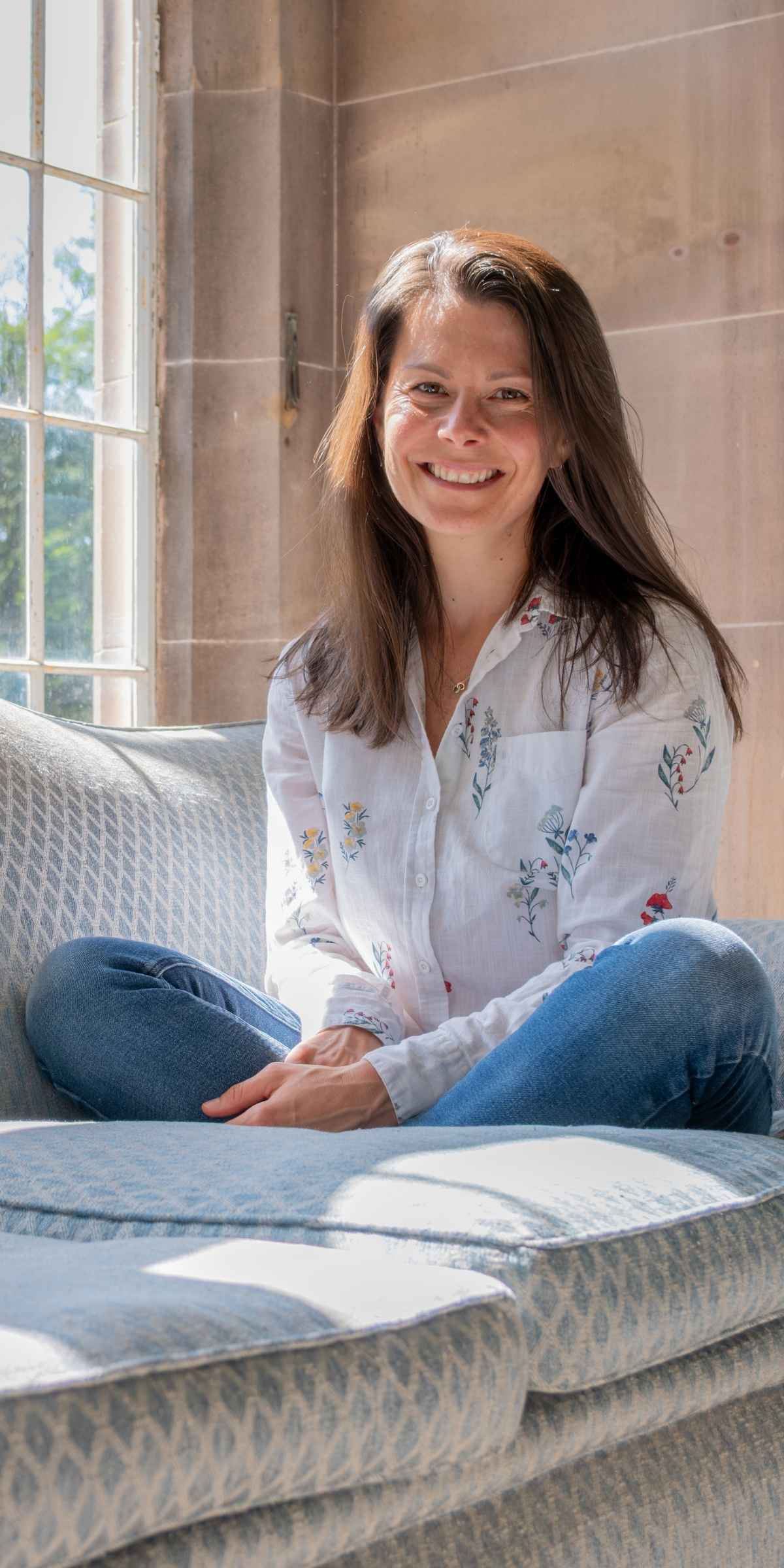 Dr Katie sat on sofa smiling, ready to help midlife women who need support with health and identity